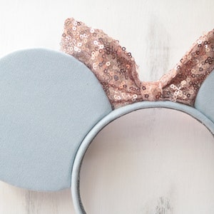Pu&ograve; includere: Fascia per capelli con orecchie di topo blu chiaro con un fiocco di paillettes oro rosa.