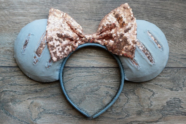 Pu&ograve; includere: Un paio di orecchie da topo in denim blu chiaro con un fiocco di paillettes oro rosa. Le orecchie hanno dettagli usurati e la fascia &egrave; nera.