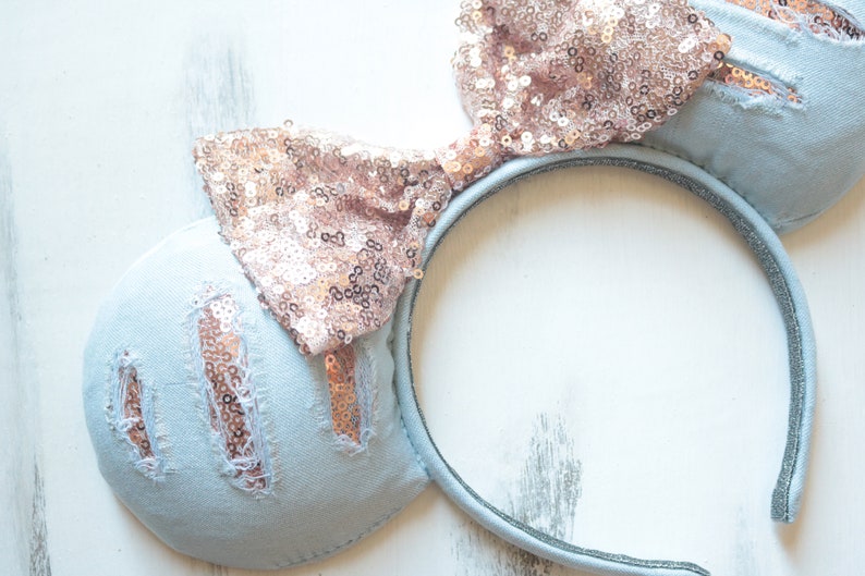 Pu&ograve; includere: Orecchie di topo in denim blu chiaro con un fiocco di paillettes oro rosa. Anche il cerchietto &egrave; in denim blu chiaro.