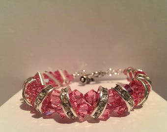 May include: A pink crystal bracelet with silver-tone accents. The bracelet features rows of faceted pink crystals, interspersed with silver-tone metal bands embellished with clear crystals. The clasp is silver-toned.