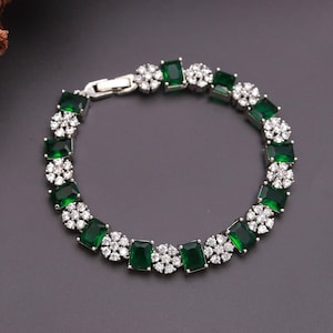 Può includere: Un bracciale color argento caratterizzato dall'alternanza di pietre rettangolari verde smeraldo e grappoli di piccole pietre rotonde bianco trasparente. Il gioiello è dotato di una chiusura in metallo e presenta un motivo ricorrente.