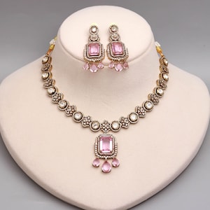 Può includere: Una collana e un paio di orecchini pendenti abbinati con montature in metallo finitura antica, pietre chiare incastonate e grandi gemme centrali rettangolari rosa chiaro, arricchite da piccole pietre rosa pendenti a forma di goccia.