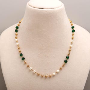 May include: A gold chain necklace featuring alternating small white pearls and dark green ribbed beads, interspersed with small gold filigree-style spherical spacers, creating a delicate and symmetrical pattern along the entire length of the jewelry.