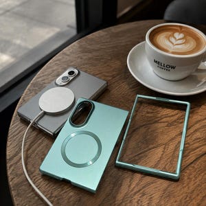 May include: A gray foldable smartphone with a white circular magnetic charger attached to the back, a light blue protective phone case with a circular magnetic ring, and a matching light blue rectangular phone frame border component.