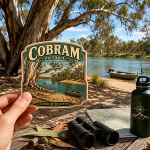 May include: A die-cut sticker featuring a scenic illustration of the Murray River in Cobram, Victoria. The artwork depicts a riverbank with large gum trees and small boats on the water. The text reads COBRAM VICTORIA ON THE MURRAY MURRAY RIVER COUNTRY.