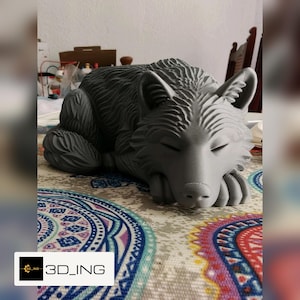 Può includere: Una statuetta stampata in 3D grigio opaco di un lupo sdraiato con gli occhi chiusi. La scultura presenta una texture dettagliata del pelo su tutto il corpo e la testa, con il lupo che appoggia la testa sulle zampe anteriori. Il testo 3D_ING è visibile.
