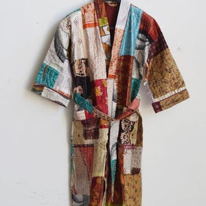 May include: A patchwork robe featuring a variety of colorful fabric squares in shades of red, blue, yellow, and brown. The garment has long sleeves, a shawl collar, and a matching fabric tie belt, all constructed with visible running stitch details.