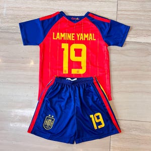 May include: A red and blue soccer jersey and shorts set featuring the name LAMINE YAMAL and the number 19 in yellow. The jersey has blue sleeves and a red body with thin vertical lines. The blue shorts display the number 19 and a team crest.