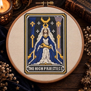 May include: A circular wooden embroidery hoop containing a cross-stitch design of The High Priestess tarot card. The figure wears a blue robe and a crescent moon crown, flanked by two pillars. The text THE HIGH PRIESTESS is stitched at the bottom.