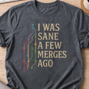 May include: A dark gray short-sleeved t-shirt featuring a graphic of a colorful branching line diagram resembling a subway map next to the text "I WAS SANE A FEW MERGES AGO" printed in a light tan, distressed, sans-serif font on the front.