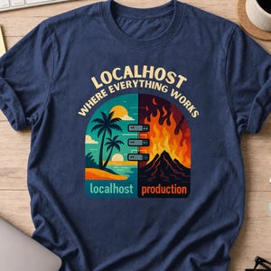 May include: A navy blue t-shirt featuring a graphic print with the text "LOCALHOST WHERE EVERYTHING WORKS". The design shows a split scene: a calm beach with palm trees labelled "localhost" and a volcanic eruption labelled "production".