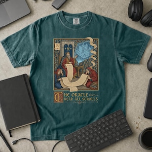 以下が含まれることがあります： ダークティールカラーの半袖Tシャツ。ローブを着た3人の人物、巻物、ノートパソコンのグラフィックイラストが描かれています。テキストは「THE ORACLE READ ALL SCROLLS」と記されています。石のアーチ、青いホログラフィック投影、複雑な花柄のデザインが含まれています。