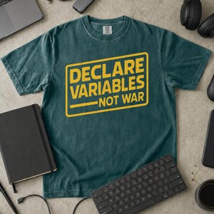 Puede incluir: Una camiseta de manga corta en color verde azulado oscuro con un gráfico rectangular amarillo de textura desgastada. El texto dentro del recuadro dice "DECLARE VARIABLES NOT WAR" en una fuente negrita sin remates, centrada en el pecho.
