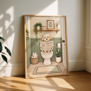 Op de afbeelding: Een ingelijste kunstprint met een lichtgekleurde, pluizige hond die op een wit toilet zit en een krant leest met de titel BARK MAIL. De badkamerscène bevat saliegroene lambrisering, een houten plank met planten en een mand met toiletpapier.