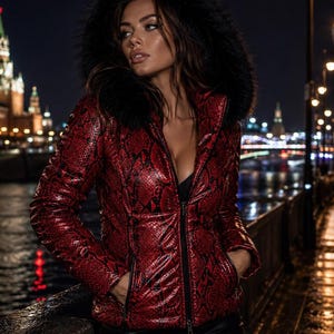 May include: A red and black snakeskin-patterned jacket featuring a high collar, a front zipper closure, and a large, dark faux fur-trimmed hood. The jacket includes two side pockets with zipper closures and long sleeves with a fitted silhouette.