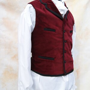 May include: A burgundy velvet vest with black trim and a white shirt underneath.