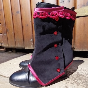 May include: Black fabric boot covers with a pink satin trim and red heart-shaped buttons. The boot covers have a lace trim at the top.