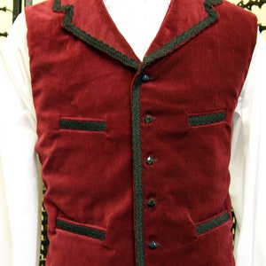 May include: A burgundy velvet vest with black trim and buttons. The vest has two pockets on the front and a pointed collar.