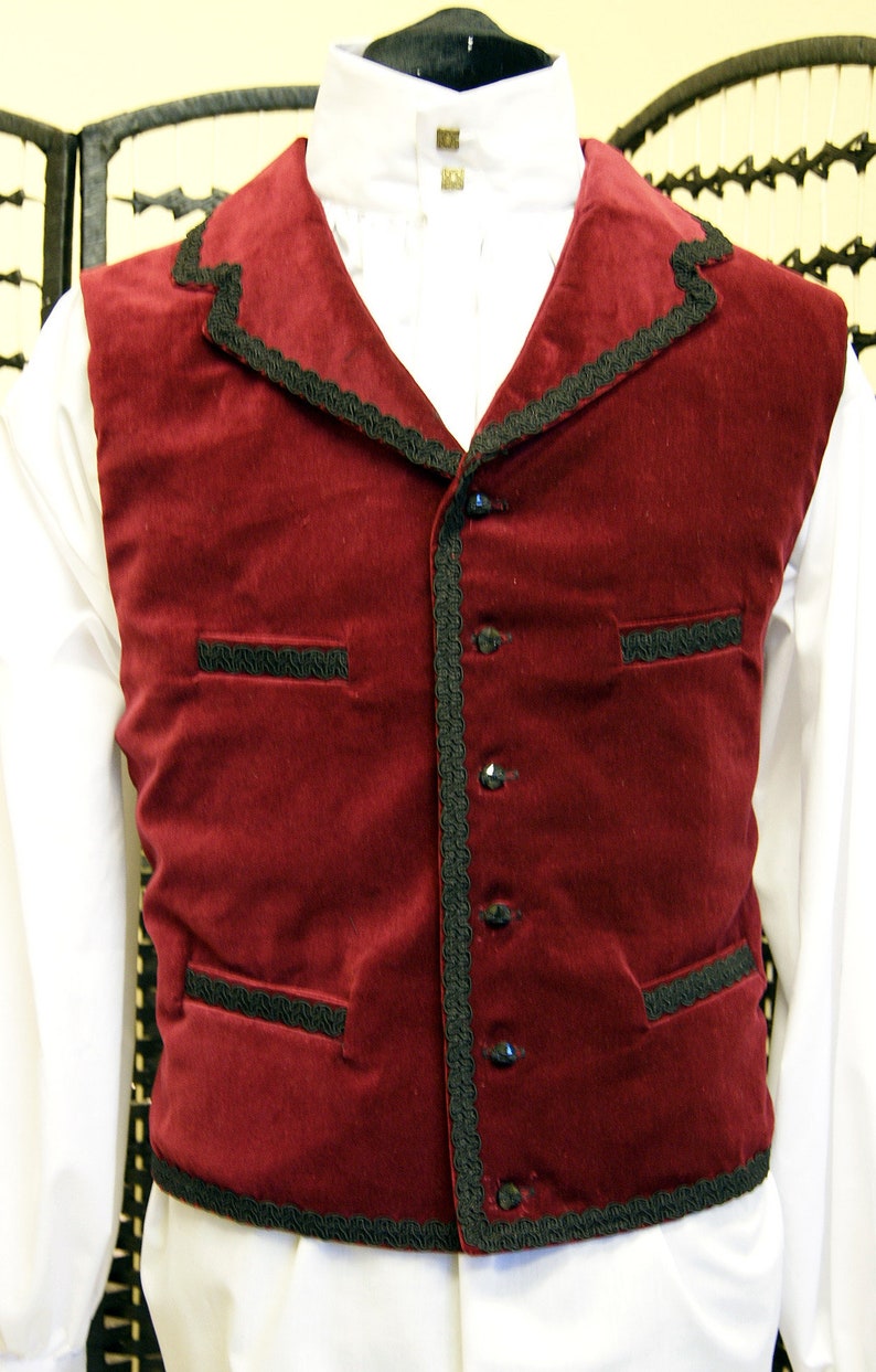 May include: A burgundy velvet vest with black trim and buttons. The vest has two pockets on the front and a pointed collar.