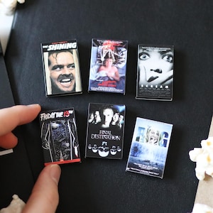 May include: Six miniature rectangular magnets featuring iconic horror movie posters including The Shining, Friday the 13th, Final Destination, and Scream. Each small rectangular piece displays detailed graphic artwork and movie titles in black, white, and colour.