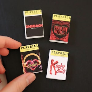 Op de afbeelding: Vier rechthoekige miniatuur Playbill-boekjes met Broadway-musicalcovers. De covers tonen titels zoals Chicago, Moulin Rouge, & Juliet en Kinky Boots. Elk boekje heeft een gele koptekst met het woord Playbill in zwarte letters.