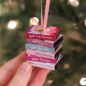 Op de afbeelding: Een miniatuurstapel van zes Barbie-filmboeken hangend aan een roze lint. De titels zijn Barbie in the Nutcracker, Barbie Rapunzel, Barbie Swan Lake, Barbie The Princess and the Pauper, Barbie Fairytopia en Barbie and the Magic of Pegasus.