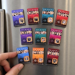 Könnte beinhalten: Ein Set aus zehn rechteckigen Magneten, die wie Miniatur-DVD-Hüllen der Fernsehserie Friends gestaltet sind, mit den Darstellern, den Staffeln eins bis zehn und dem ikonischen gelben Bilderrahmen um eine kleine Szene.