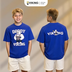 May include: A royal blue short-sleeved t-shirt featuring a pixel art graphic of a muscular white bear wearing a tank top. The front displays the text "DADDY VIKING" in white pixelated font, while the back shows "VIKING" with a bear graphic.