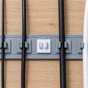 Könnte beinhalten: Ein grauer, rechteckiger Kabelorganizer mit fünf Schlitzen zur Kabelführung. Der mittlere Schlitz ist weiß und mit den Buchstaben WS versehen. Vier schwarze und weiße Kabel stecken in den Schlitzen, die mit 3, 4, 5 und 7 beschriftet sind.