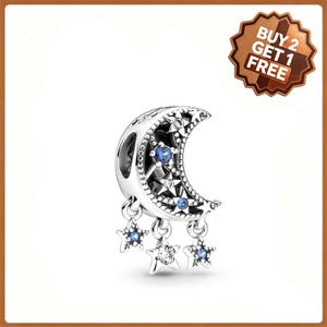 May include: A silver-toned crescent moon charm featuring embedded clear and blue stones, with three dangling star-shaped charms also accented with clear and blue stones. A brown badge in the corner displays the text BUY 2 GET 1 FREE.