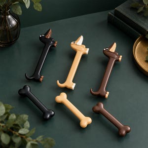 May include: Three dachshund-shaped drawer pulls and three bone-shaped drawer pulls in black, tan, and dark brown colors. Each dachshund figure features a long body, upright ears, and a curled tail, while the bone figures have rounded ends.