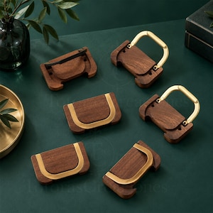 May include: Six rectangular drawer pulls featuring dark brown wood bases with smooth, polished gold-toned metal U-shaped handles. The hardware pieces are arranged in a scattered pattern, showcasing both the flat wood surfaces and the raised metal handles.