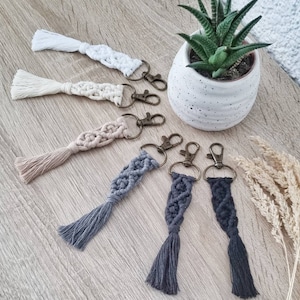 Puede incluir: Seis llaveros de macramé hechos a mano con borlas en blanco, beige, gris y negro. Los llaveros están unidos a llaveros de plata.