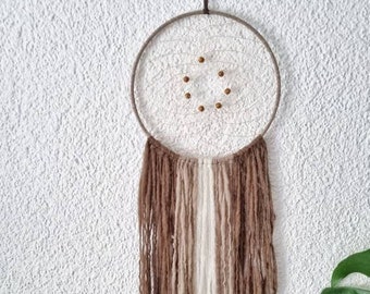 May include: A brown and white yarn dream catcher with a wooden ring and brown beads hanging from a white wall.