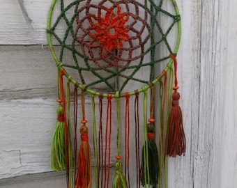 May include: A green, brown, and orange dreamcatcher with a beaded string and tassels hanging from the bottom.