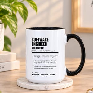 May include: A white ceramic mug with a black interior and handle, featuring black printed text that defines a software engineer as a code architect, including bullet points about building software, solving problems, and shaping the future.