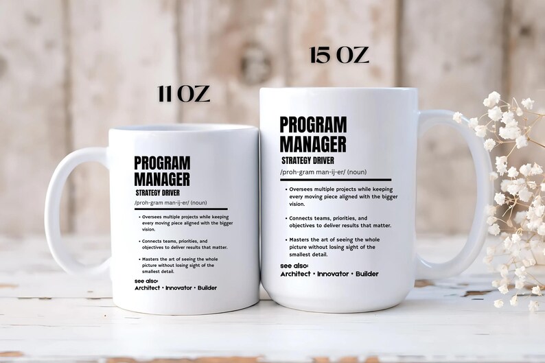 May include: Two white ceramic mugs with black text. The smaller mug is labeled 11 OZ and the larger mug is labeled 15 OZ. Both feature the definition of a Program Manager, including the text Strategy Driver, and see also: Architect, Innovator, Builder.