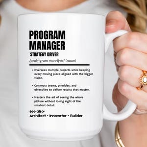 May include: A white ceramic mug featuring black text that defines a Program Manager as a strategy driver. The text includes a phonetic pronunciation, a noun classification, three bulleted job responsibilities, and a see also section listing Architect, Innovator, and Builder.