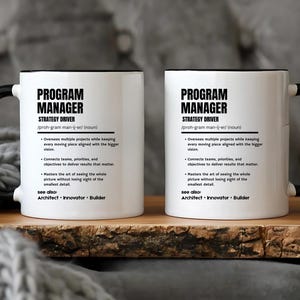 May include: Two white ceramic mugs with black handles and rims, each featuring black printed text that defines a program manager as a strategy driver, including bulleted job responsibilities and a see also section listing architect, innovator, and builder.