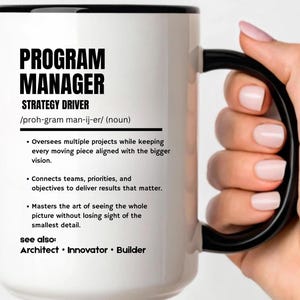 May include: A white ceramic mug with a black rim and handle, featuring black text that defines a Program Manager as a strategy driver, including bulleted descriptions of the role and a list of related titles like Architect, Innovator, and Builder.