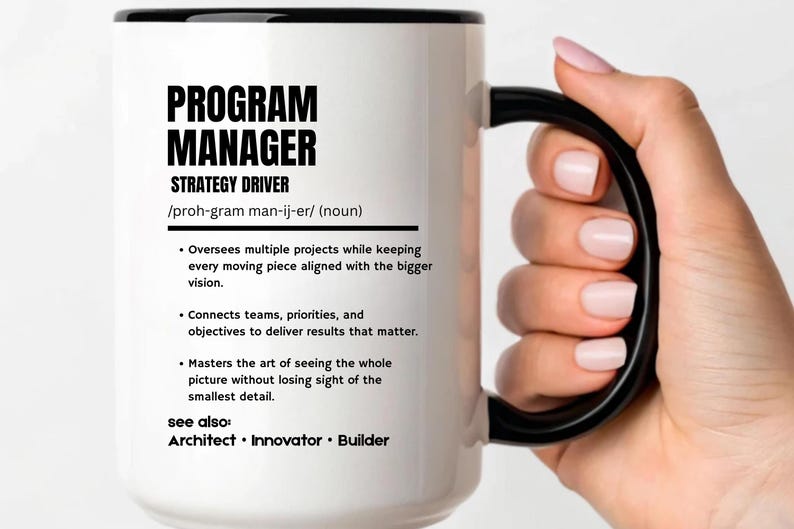 May include: A white ceramic mug with a black rim and handle, featuring black text that defines a Program Manager as a strategy driver, including bulleted descriptions of the role and a list of related titles like Architect, Innovator, and Builder.