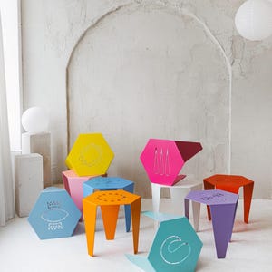 Könnte beinhalten: Eine Sammlung sechseckiger Metallhocker in verschiedenen leuchtenden Farben wie Gelb, Pink, Blau, Orange, Lila und Türkis. Jeder Hocker weist auf seiner Ober- oder Seitenfläche ein einzigartiges, lasergeschnittenes Design auf, wie geometrische Formen.