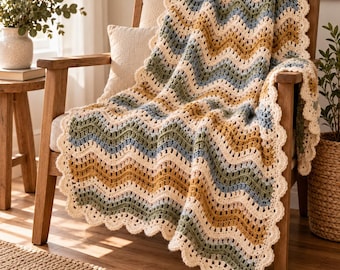 May include: A crocheted blanket featuring a wavy chevron pattern in alternating stripes of cream, sage green, dusty blue, and mustard yellow. The blanket has a scalloped edge border in cream and is draped over a wooden chair with a cream pillow.