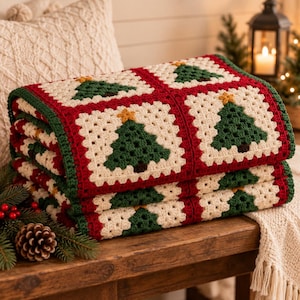 May include: A handmade crochet blanket featuring a repeating granny square pattern. Each square displays a dark green Christmas tree with a yellow star on top, set against a cream-colored background, all bordered by deep red and green yarn.