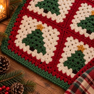 May include: A crocheted blanket featuring a repeating granny square pattern. Each square displays a dark green Christmas tree with a yellow star on top, set against a cream-colored background, all bordered by a vibrant red and green yarn frame.