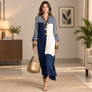 May include: A long-sleeved shirt dress featuring a color-blocked design with navy blue, cream, and navy-and-white vertical stripes. The dress has a collared neckline, button-down front, and ruffled cuffs. It is accessorized with a long beaded necklace.