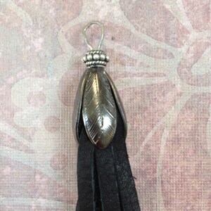 K&ouml;nnte beinhalten: Ein schwarzer Lederquaste mit einem silbernen Metallkopf. Der Kopf hat ein dekoratives Blattdesign.