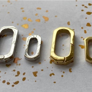 May include: Three silver and gold metal clasps, each with a different size. The clasps are rectangular in shape and have a smooth, polished finish.