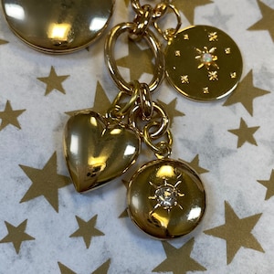 May include: A gold charm bracelet with a variety of charms, including a heart, a locket, and a star. The charms are attached to a gold chain.