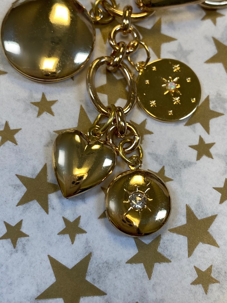 May include: A gold charm bracelet with a variety of charms, including a heart, a locket, and a star. The charms are attached to a gold chain.